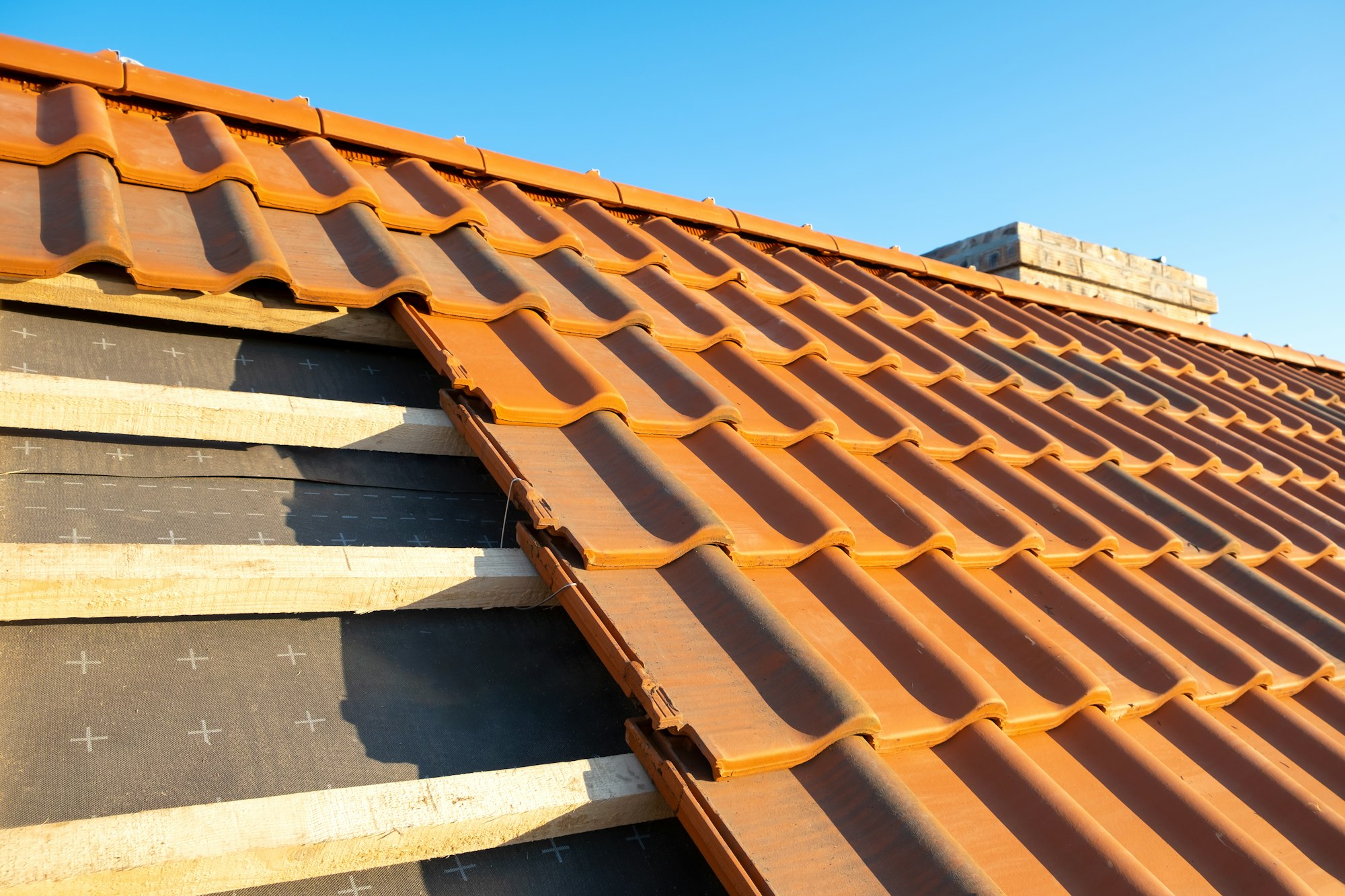 Overlapping rows of yellow ceramic roofing tiles mounted on wooden boards covering residential