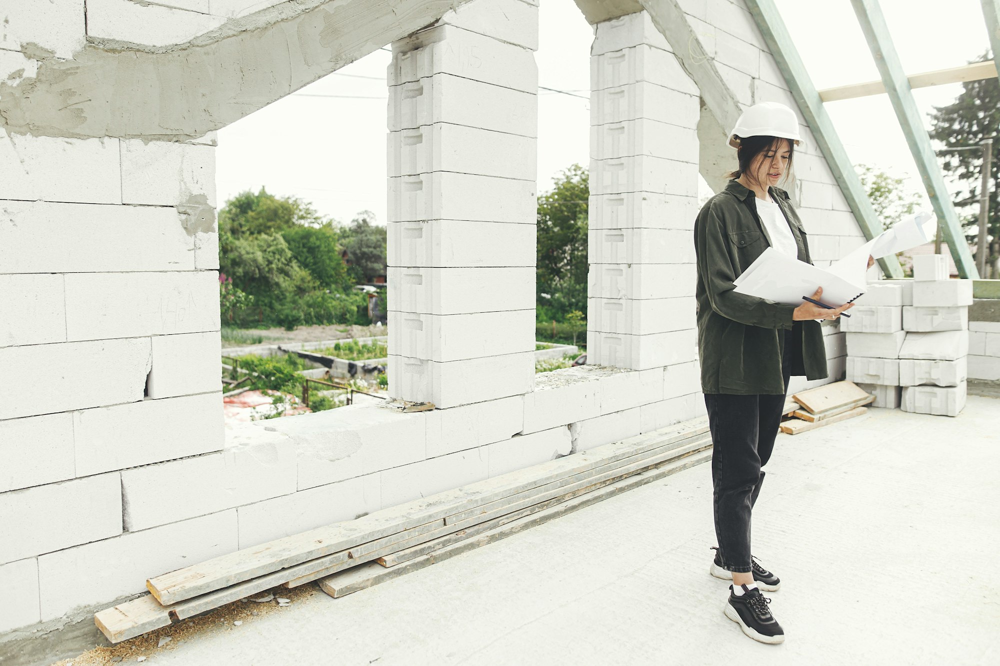 Stylish happy woman architect checking blueprints against wooden roof framing of modern farmhouse